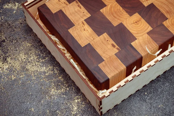 End cutting board on a dark textured background. Kitchen utensils made of natural wood. Expensive vintage items. Luxurious quality woodworking. Chess pattern on a wooden board