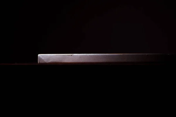 Side view of the canvas stretched on a stretcher. The concept of the modern school of art. Dark background. The work of art lies on a wooden table.