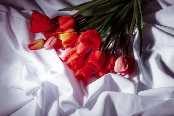 Natural bouquet of spring tulips. Red tulips on a smart white background. Valentine's day, mother's day, tenderness day, birthday concept. Flowers on the bed linen. Soft selective focus. Spring scene.