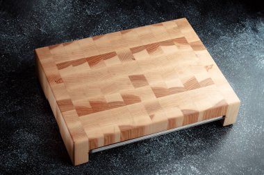 Koyu dokulu arka planda kesme tahtası. Doğranmış sebzeler, et ve diğer ürünler için paslanmaz tepsi. Lüks kaliteli ahşap işçiliği. Tahtada satranç deseni.