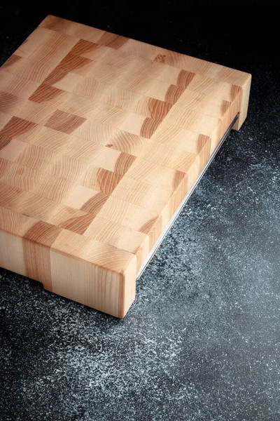 End cutting board on a dark textured background. Stainless tray for chopped vegetables, meat and other products. Luxurious quality woodworking. Chess pattern on a wooden board.