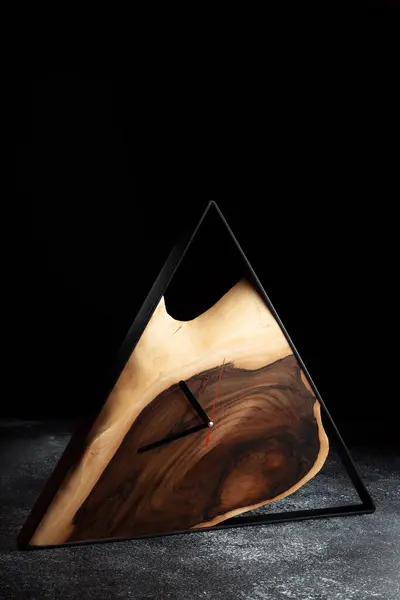 Koyu gri arka planda tahta üçgen duvar saati. Ev, ofis ya da restoran için lüks aksesuarlar. Çatı katı tarzı ahşap ve epoksi. İş tarzı arkaplanı.