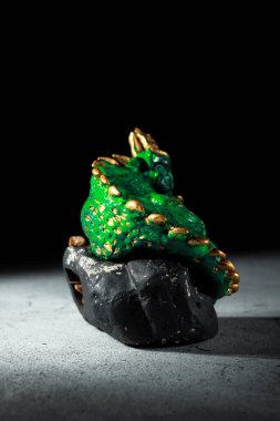 Büyük bir taşın üzerinde altın çivileri olan yeşil bir ejderha. 2024 sembolünün heykeli. Karanlık bir arkaplan ve bir yazı için boşluk. Çin Yeni Yılı için davetiye.