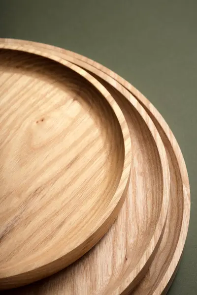 Koyu yeşil arka planda tahta düz plakalar. Ekolojik sofra takımı kavramı. Modern mutfak ürünleri. Doğal uyum: Çevre dostu bir mutfakta ahşap tabaklar. Sıcak lamba gölgeleri.