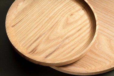 Koyu yeşil arka planda tahta düz plakalar. Ekolojik sofra takımı kavramı. Modern mutfak ürünleri. Doğal uyum: Çevre dostu bir mutfakta ahşap tabaklar. Sıcak lamba gölgeleri.