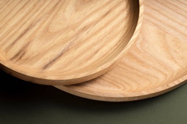 Koyu yeşil arka planda tahta düz plakalar. Ekolojik sofra takımı kavramı. Modern mutfak ürünleri. Doğal uyum: Çevre dostu bir mutfakta ahşap tabaklar. Sıcak lamba gölgeleri.