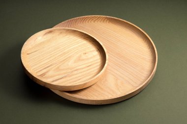 Koyu yeşil arka planda tahta düz plakalar. Ekolojik sofra takımı kavramı. Modern mutfak ürünleri. Doğal uyum: Çevre dostu bir mutfakta ahşap tabaklar. Sıcak lamba gölgeleri.