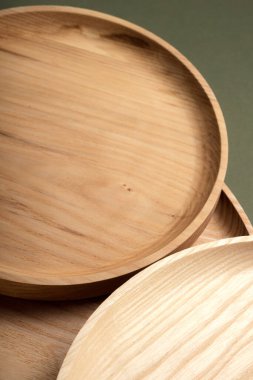 Koyu yeşil arka planda tahta düz plakalar. Ekolojik sofra takımı kavramı. Modern mutfak ürünleri. Doğal uyum: Çevre dostu bir mutfakta ahşap tabaklar. Sıcak lamba gölgeleri.