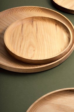Koyu yeşil arka planda tahta düz plakalar. Ekolojik sofra takımı kavramı. Modern mutfak ürünleri. Doğal uyum: Çevre dostu bir mutfakta ahşap tabaklar. Sıcak lamba gölgeleri.