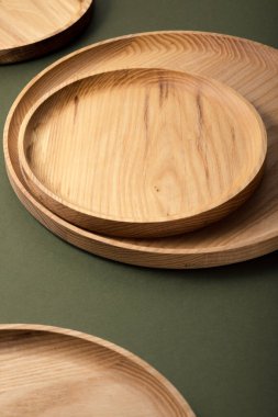 Koyu yeşil arka planda tahta düz plakalar. Ekolojik sofra takımı kavramı. Modern mutfak ürünleri. Doğal uyum: Çevre dostu bir mutfakta ahşap tabaklar. Sıcak lamba gölgeleri.