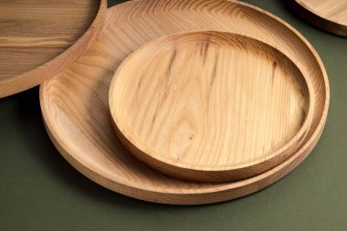 Koyu yeşil arka planda tahta düz plakalar. Ekolojik sofra takımı kavramı. Modern mutfak ürünleri. Doğal uyum: Çevre dostu bir mutfakta ahşap tabaklar. Sıcak lamba gölgeleri.