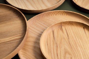 Koyu yeşil arka planda tahta düz plakalar. Ekolojik sofra takımı kavramı. Modern mutfak ürünleri. Doğal uyum: Çevre dostu bir mutfakta ahşap tabaklar. Sıcak lamba gölgeleri.