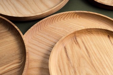 Koyu yeşil arka planda tahta düz plakalar. Ekolojik sofra takımı kavramı. Modern mutfak ürünleri. Doğal uyum: Çevre dostu bir mutfakta ahşap tabaklar. Sıcak lamba gölgeleri.