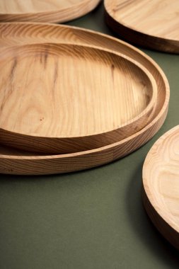 Koyu yeşil arka planda tahta düz plakalar. Ekolojik sofra takımı kavramı. Modern mutfak ürünleri. Doğal uyum: Çevre dostu bir mutfakta ahşap tabaklar. Sıcak lamba gölgeleri.