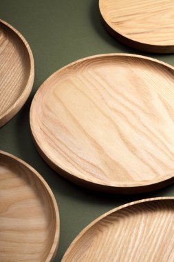 Koyu yeşil arka planda tahta düz plakalar. Ekolojik sofra takımı kavramı. Modern mutfak ürünleri. Doğal uyum: Çevre dostu bir mutfakta ahşap tabaklar. Sıcak lamba gölgeleri.