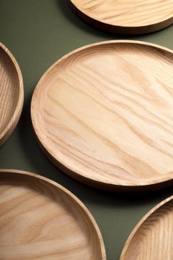Koyu yeşil arka planda tahta düz plakalar. Ekolojik sofra takımı kavramı. Modern mutfak ürünleri. Doğal uyum: Çevre dostu bir mutfakta ahşap tabaklar. Sıcak lamba gölgeleri.