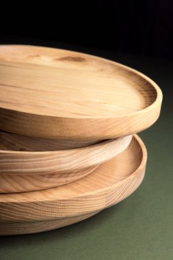 Koyu yeşil arka planda tahta düz plakalar. Ekolojik sofra takımı kavramı. Modern mutfak ürünleri. Doğal uyum: Çevre dostu bir mutfakta ahşap tabaklar. Sıcak lamba gölgeleri.