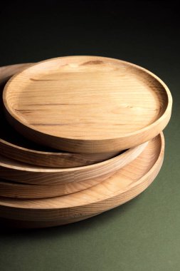 Koyu yeşil arka planda tahta düz plakalar. Ekolojik sofra takımı kavramı. Modern mutfak ürünleri. Doğal uyum: Çevre dostu bir mutfakta ahşap tabaklar. Sıcak lamba gölgeleri.