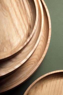 Koyu yeşil arka planda tahta düz plakalar. Ekolojik sofra takımı kavramı. Modern mutfak ürünleri. Doğal uyum: Çevre dostu bir mutfakta ahşap tabaklar. Sıcak lamba gölgeleri.