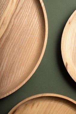 Koyu yeşil arka planda tahta düz plakalar. Ekolojik sofra takımı kavramı. Modern mutfak ürünleri. Doğal uyum: Çevre dostu bir mutfakta ahşap tabaklar. Sıcak lamba gölgeleri.