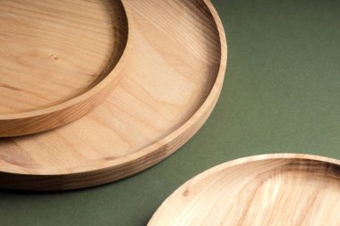 Koyu yeşil arka planda tahta düz plakalar. Ekolojik sofra takımı kavramı. Modern mutfak ürünleri. Doğal uyum: Çevre dostu bir mutfakta ahşap tabaklar. Sıcak lamba gölgeleri.