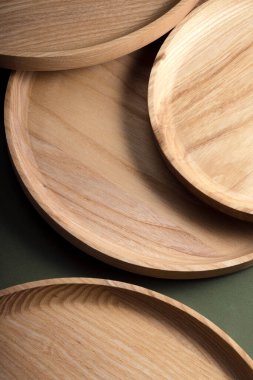 Koyu yeşil arka planda tahta düz plakalar. Ekolojik sofra takımı kavramı. Modern mutfak ürünleri. Doğal uyum: Çevre dostu bir mutfakta ahşap tabaklar. Sıcak lamba gölgeleri.