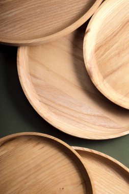 Koyu yeşil arka planda tahta düz plakalar. Ekolojik sofra takımı kavramı. Modern mutfak ürünleri. Doğal uyum: Çevre dostu bir mutfakta ahşap tabaklar. Sıcak lamba gölgeleri.