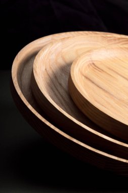 Koyu yeşil arka planda tahta düz plakalar. Ekolojik sofra takımı kavramı. Modern mutfak ürünleri. Doğal uyum: Çevre dostu bir mutfakta ahşap tabaklar. Sıcak lamba gölgeleri.