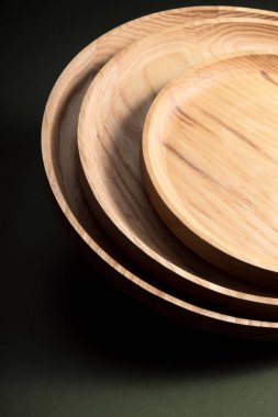 Koyu yeşil arka planda tahta düz plakalar. Ekolojik sofra takımı kavramı. Modern mutfak ürünleri. Doğal uyum: Çevre dostu bir mutfakta ahşap tabaklar. Sıcak lamba gölgeleri.