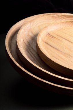 Koyu yeşil arka planda tahta düz plakalar. Ekolojik sofra takımı kavramı. Modern mutfak ürünleri. Doğal uyum: Çevre dostu bir mutfakta ahşap tabaklar. Sıcak lamba gölgeleri.