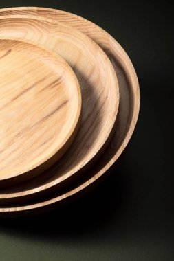 Koyu yeşil arka planda tahta düz plakalar. Ekolojik sofra takımı kavramı. Modern mutfak ürünleri. Doğal uyum: Çevre dostu bir mutfakta ahşap tabaklar. Sıcak lamba gölgeleri.