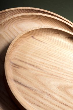 Koyu yeşil arka planda tahta düz plakalar. Ekolojik sofra takımı kavramı. Modern mutfak ürünleri. Doğal uyum: Çevre dostu bir mutfakta ahşap tabaklar. Sıcak lamba gölgeleri.