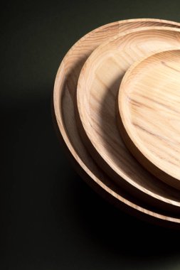 Koyu yeşil arka planda tahta düz plakalar. Ekolojik sofra takımı kavramı. Modern mutfak ürünleri. Doğal uyum: Çevre dostu bir mutfakta ahşap tabaklar. Sıcak lamba gölgeleri.