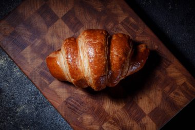 Tahta kesme tahtasının üzerinde taze pişmiş kruvasan. Koyu arkaplanda Fransız hamur işi ürünleri. Kahvaltı ve kahve fikir kırıyor..