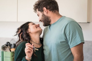 A young married couple rejoices over the purchase of the new house - the two newlywed young people look into each other's eyes and hold the keys to the apartment - people lifestyle concept