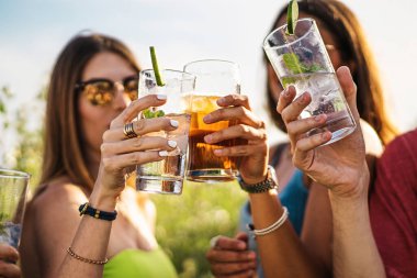 Cheerful group of millennial friends toasting alcoholic cocktails in the summer - people gathering cheering and drinking alcoholic drinks lifestyle concept