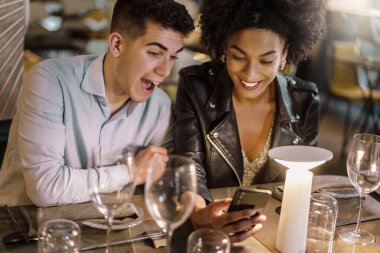 Mutlu çok ırklı çift akıllı cep telefonuyla gülüyor sosyal ağ içeriğini izliyor ve eğleniyor - birlik ve çeşitlilik insanları ve teknoloji yaşam tarzı konsepti -