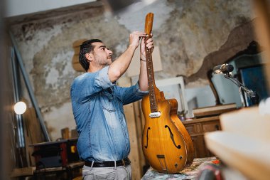 Luthier bir gitarı tamir ediyor. Klasik stüdyo garajında çubukla düzüşüyor. Müzik, sanat, el sanatları ve insan yaşam tarzı konsepti.