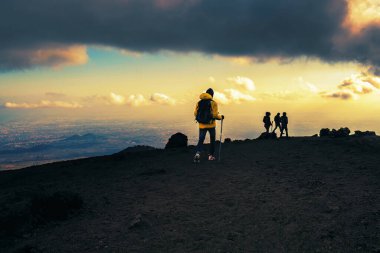 Gün batımında İtalya, Sicilya 'daki Etna Dağı' nın lav taşında yürüyen bir grup yürüyüşçü tanınmayan insanlar bulutlu bir gökyüzünden görüyorlar. Seyahat, doğa, insan yaşam tarzı kavramı.