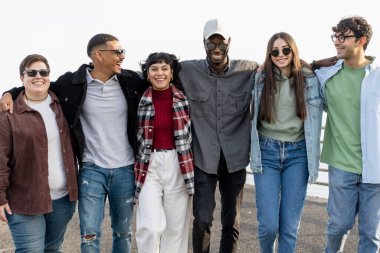 En iyi çok ırklı genç arkadaşlar yürür ve tasasız kollarıyla konuşurlar - deniz kenarında kucaklaşan bir grup çok ırklı insan - insanlar, arkadaşlık, birlik, entegrasyon ve yaşam tarzı kavramı