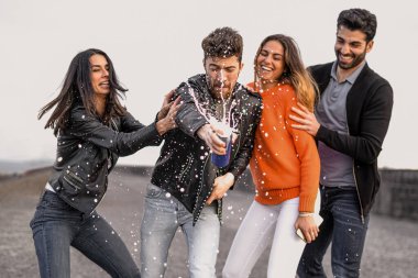 An excited group of friends have fun opening a can of beer, making the foam splash everywhere - youth people lifestyle concept.