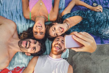 Dört genç yetişkin plajda gün boyu eğleniyor, havluların üzerinde uzanıyor ve grup selfie 'si çekiyor. Gülerek ve aptalca suratlar yaparak arkadaşlarıyla geçirdikleri mükemmel bir yaz gününün neşe ve hatıralarını yakalıyorlar.