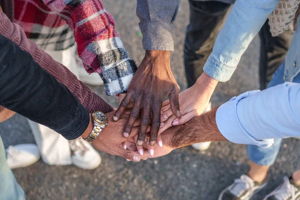 A group of friends join hands in a circle, representing unity and friendship. The close-up image focuses on their hands, display a variety of ethnicities, including a young African man\'s hand on top