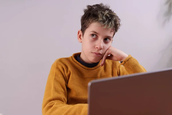 ラップトップコンピュータを使用して若い子供のクローズアップショット 子供は深く考えられているように見え 目は上を見上げ 手に頭を休める ノートパソコンの画面は前景に表示され 少しぼやけて焦点が外れています — ストック写真