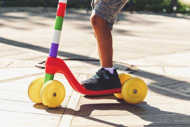 Oyuncak scooter kullanan bir çocuğun bacak ve ayaklarının detaylı görüntüsü. Tanımlanamayan çocuk şort ve spor ayakkabı giyiyor..