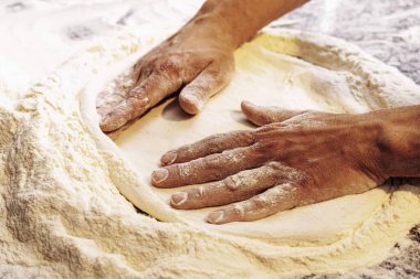 Bir pizzacının ellerini kapayarak pizza hamurunu ustalıkla un kaplı bir yüzeye uzatarak geleneksel pizza yapma sanatını yakalıyor..