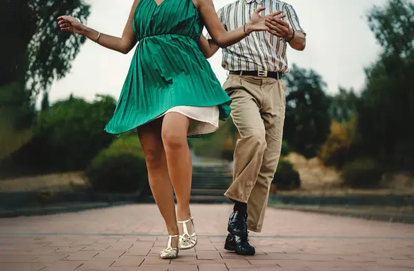 Close-up of a couple\'s feet and attire while performing swing dance moves outdoors. Authentic swing shoes and clothing details.