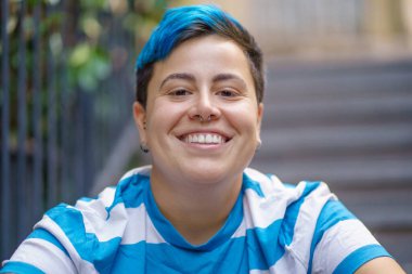 Renkli mavi saçlı neşeli bir gencin yakın plan portresi şehir korkuluklarına ve merdivenlere karşı poz veriyor.