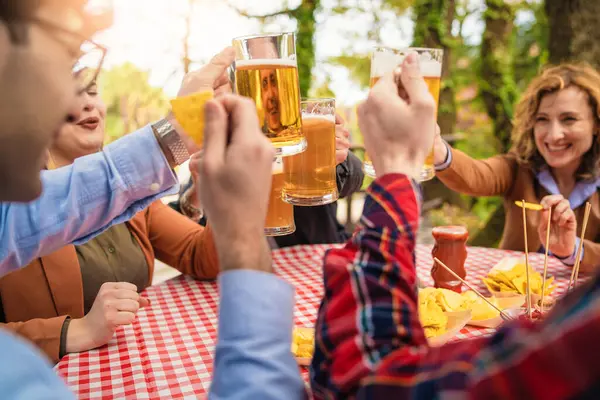 A multiracial group of five male friends comes together outdoors, raising their beer mugs in a toast. Their faces light up with joy as they share this moment, all smiles directed towards the camera.