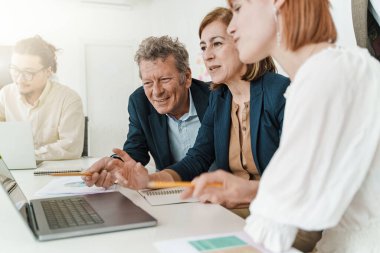 Üst düzey ve alt düzey üç meslektaş, bir dizüstü bilgisayarın ekranını gözlemleyerek ortak bir tartışmaya giriştiler. Onların odaklanmış ifadeleri takım çalışmasının ve bilgi paylaşımının önemini vurgular..